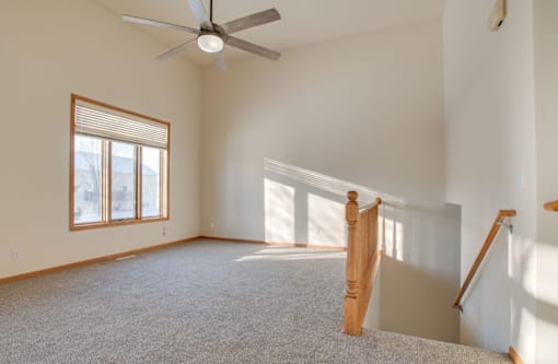 A room with a carpeted floor, a ceiling fan, and a window with blinds.