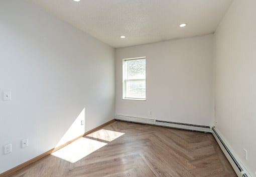 A room with wooden flooring and a window letting in sunlight.