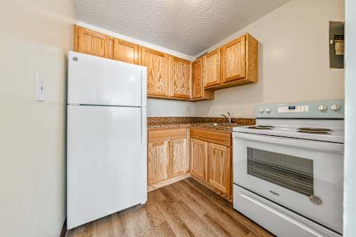 A white refrigerator stands in a kitchen with wooden cabinets and a white oven at 500 Manila Senior Apartments in Jersey City