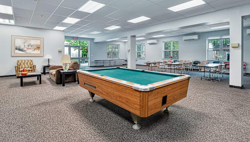 A pool table is in the middle of a room with chairs and a painting on the wall.