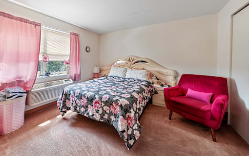 A bedroom with a floral bedspread and a red chair.