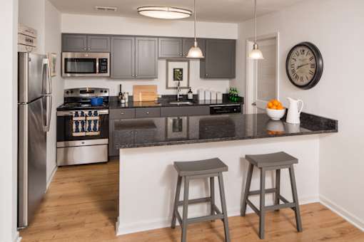 Kitchen with dark cabinets, quartz counters, and a peninsula with two chairs behind it.