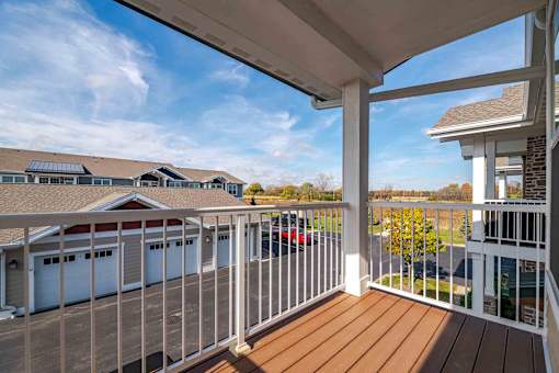 A white railing on a wooden deck with a view of a house and cars.