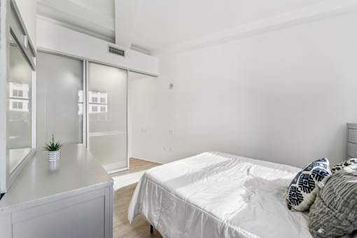A bedroom with a bed, nightstand, and a plant on the counter.