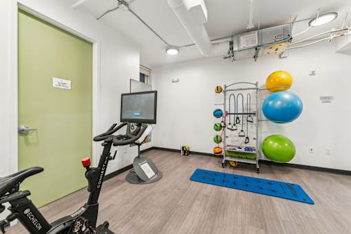 A gym room with a stationary bike, a row of exercise balls, and a rack of resistance bands.