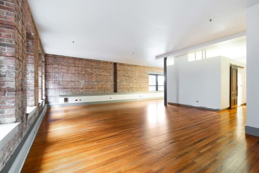 an empty living room with wood floors and a brick wall
