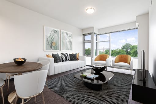A modern living room with a white sofa, a wooden table, and a large window.