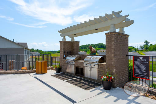 two stainless steel bbq grills on a patio with a pergola