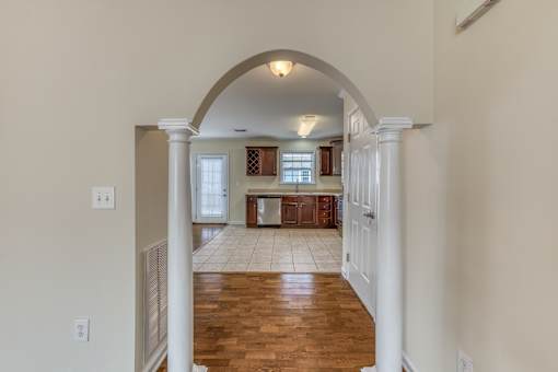 A hallway with a white archway leading to a kitchen.