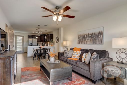 A living room with white walls, hardwood style vinyl flooring, and a kitchen visible in the background.