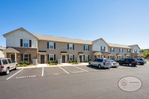 A tan, one story apartment building with ample parking.
