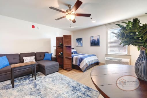 A studio apartment, living and sleeping area with white walls and hardwood style vinyl flooring.