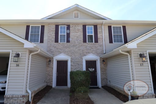 The front of a tan brick house with two maroon doors.