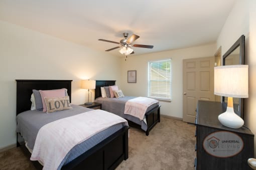 A bedroom with two beds, carpet, white walls, and a ceiling fan