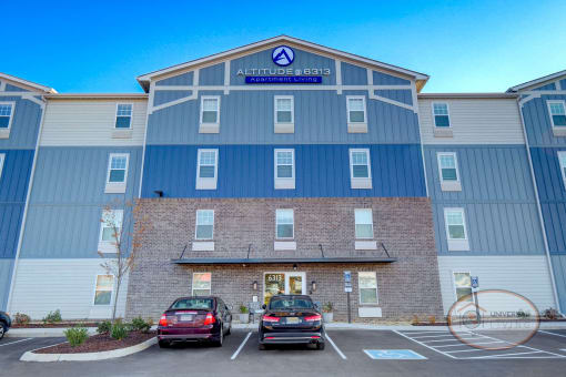 Exterior view of a grey and blue apartment home complex with ample parking.