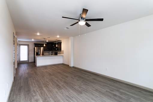 A spacious living room with a ceiling fan and a kitchen area in the background.