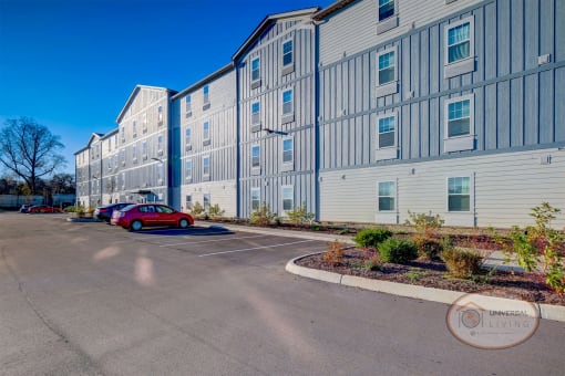 Exterior view of a grey and blue apartment home complex with ample parking.