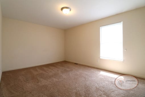 An empty bedroom with tan carpet and a large window.