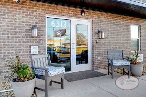A close up of the front door with a brick accent wall and outdoor seating.