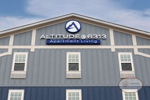 The sign on the top of the blue and grey apartment building that reads "Altitude @ 6313 Apartment Living."