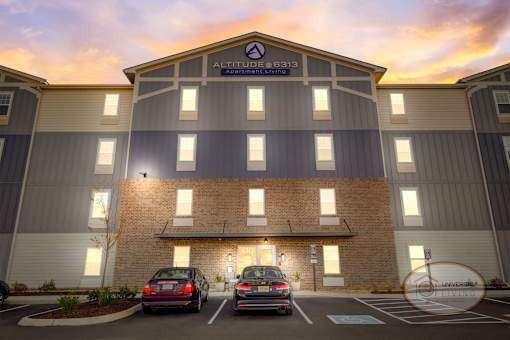 The front of a blue and grey apartment building at sunset with stone accents and a sign that reads