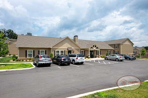 The tan clubhouse exterior with cars parked in front.