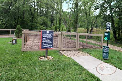 A fenced in dog park with obstacles, a water fountain for pets, and a bench.