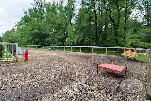 A fenced in dog park with obstacles, a water fountain for pets, and a bench.