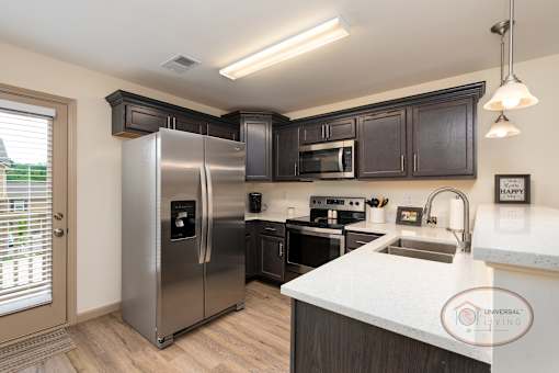 A kitchen with hardwood vinyl flooring, white walls, dark cabinets, and stainless steel appliances.