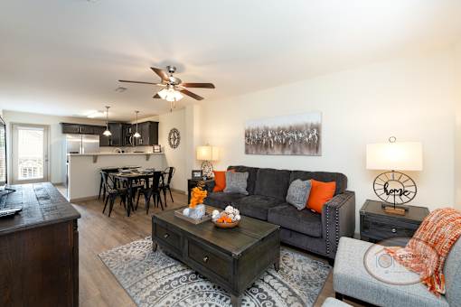 A living room with a grey couch and a coffee table, hardwood vinyl flooring, and a kitchen in the background.
