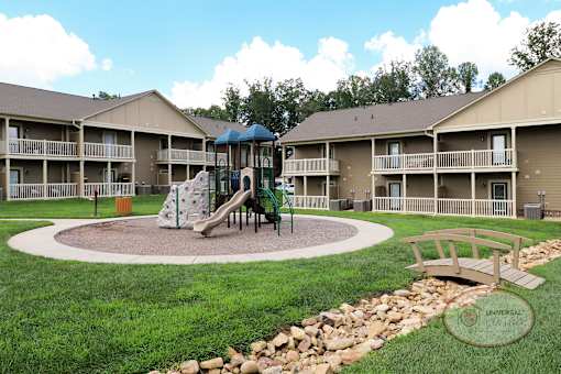A playground area with a slide and a wooden bench in front of apartment buildings.
