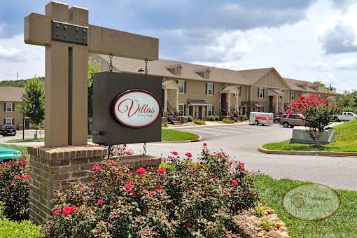A sign for The Villas at Avery Creek in front of the clubhouse surrounded by red flowers.
