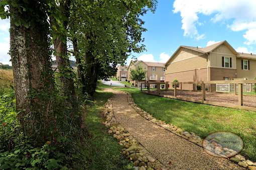 A gravel walkway leading past a row of apartment buildings to a dog park and a firepit.
