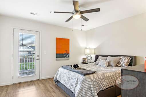 A bedroom with a bed, a ceiling fan, and a glass door leading onto a balcony/patio.