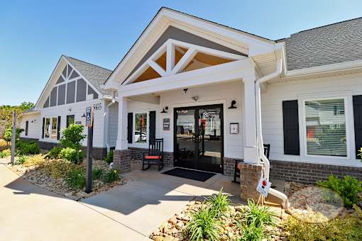 The front of the grey and white clubhouse with green plants and rocking chairs on the porch.