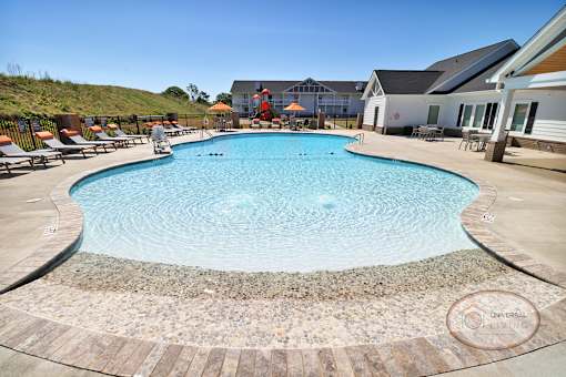 A large swimming pool surrounded by lounge chairs with apartment buildings in the background.