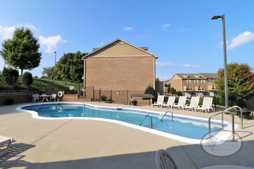 A swimming pool with lounge chairs and apartment buildings in the background.