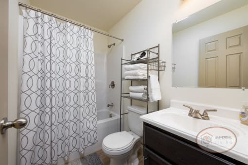 A bathroom with a shower over tub, white counters, and dark cabinets.