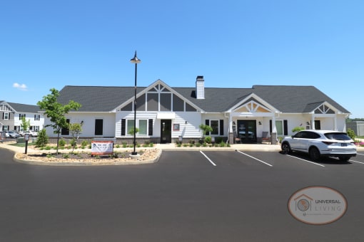 A white and grey clubhouse and leasing office with large parking lot.