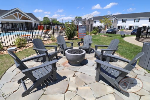 A fire pit surrounded by grey Adirondack chairs.