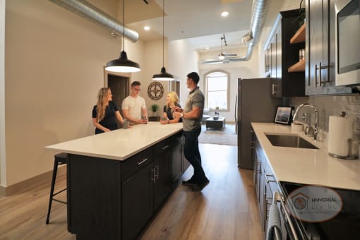 A group of friends gathered around a black kitchen island with white countertops.