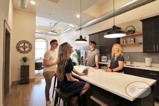A group of friends gathered around a black kitchen island with white countertops.