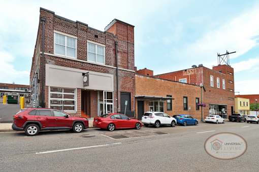 A line of cars parked in front of a historic brick apartment building along a downtown street.