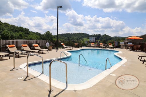 A resort style saltwater swimming pool with zero entry, lounge chairs, grills, and the clubhouse in the background.