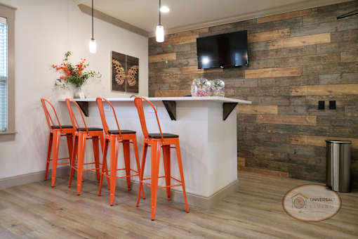 A coffee bar inside the clubhouse lounge with orange bar stool seating and a flat screen TV on a wooden accent wall.