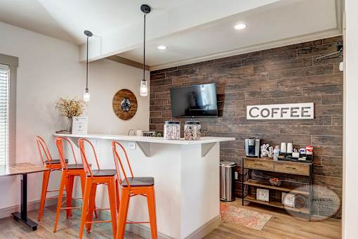 A coffee bar with orange chairs, flat screen TV,  and a brick accent wall.