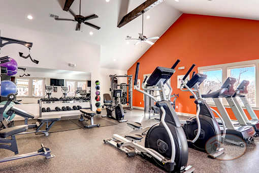 A gym with an orange accent wall and a variety of exercise equipment.