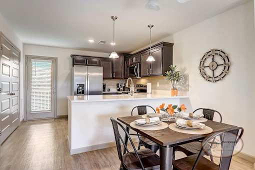 A kitchen with a dining area in front, hardwood vinyl floors, white counter tops, dark cabinets, a door to the patio, and stainless steel appliances.