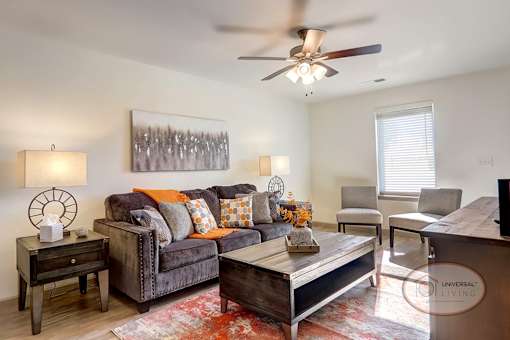 A fully furnished living room with hardwood vinyl flooring, white walls, and a ceiling fan.