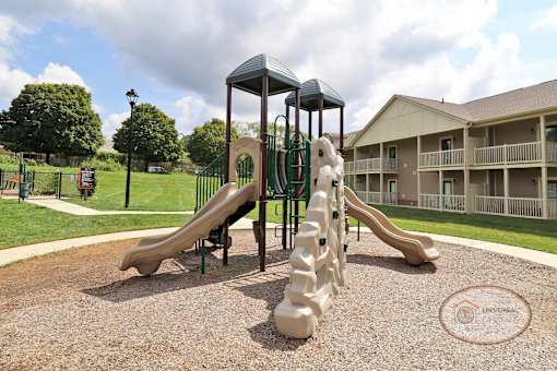 A playground with a slide and jungle gym in front of a row of apartments.